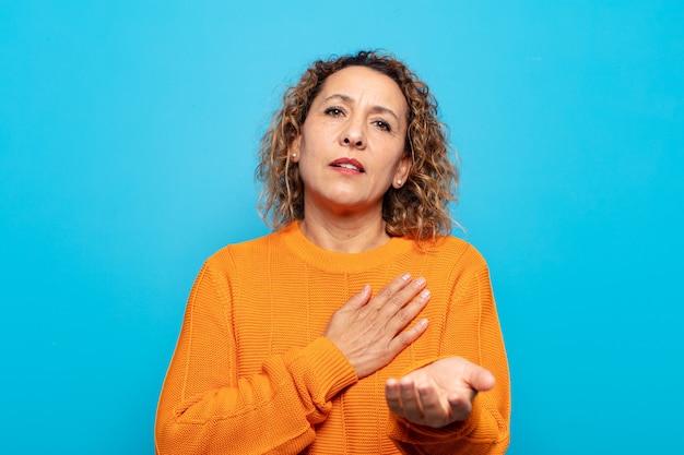 Mujer de mediana edad que se siente feliz y enamorada, sonriendo con una mano al lado del corazón y la otra estirada al frente