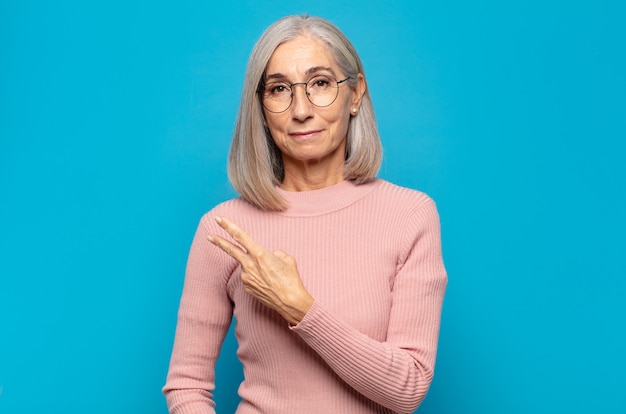 Mujer de mediana edad que se siente feliz, positiva y exitosa, con la mano haciendo forma de v sobre el pecho