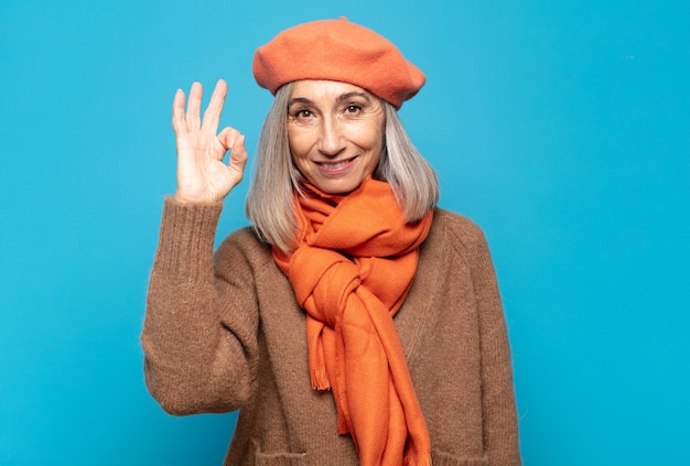 Mujer de mediana edad que se siente feliz, relajada y satisfecha, mostrando aprobación con gesto bien, sonriendo