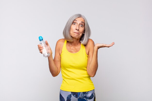 Mujer de mediana edad que se siente perpleja y confundida, dudando, ponderando o eligiendo diferentes opciones con expresión divertida. concepto de fitness