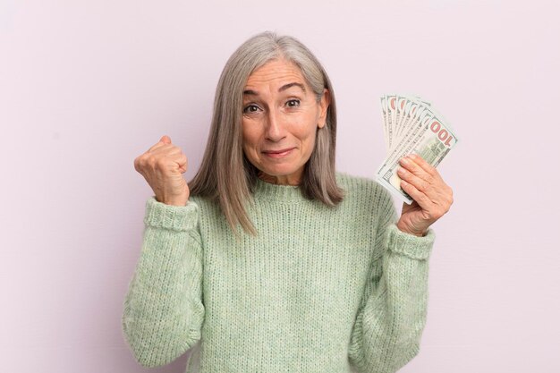 Mujer de mediana edad que se siente sorprendida, riendo y celebrando el éxito del concepto de billetes en dólares