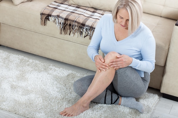 Mujer de mediana edad que sufre de dolor en la pierna en casa.