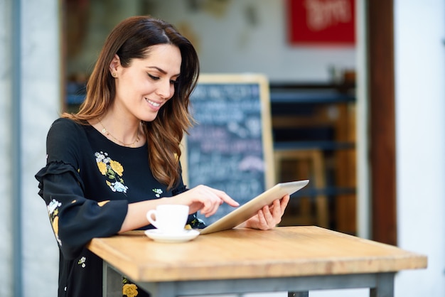 Mujer de mediana edad que usa la tableta en descanso para tomar café en barra urbana del café.