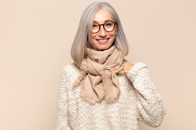 Mujer de mediana edad que se ve feliz, orgullosa y sorprendida, alegremente apuntando a sí misma, sintiéndose segura y elevada