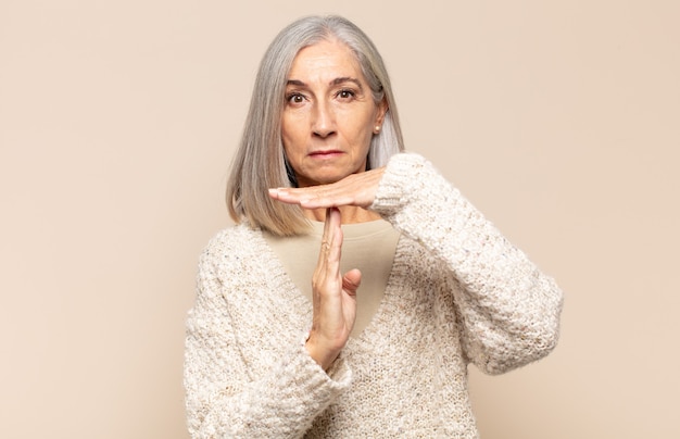 Mujer de mediana edad que se ve seria, severa, enojada y disgustada, haciendo el signo de tiempo de espera