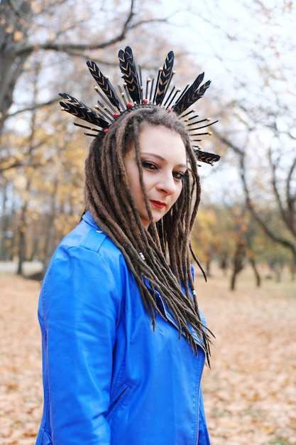 Una mujer de mediana edad con rastas y un aro en el pelo con plumas camina en el parque de otoño