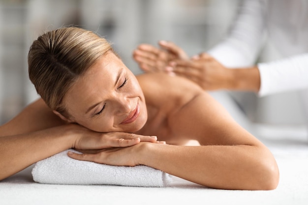 Mujer de mediana edad relajada recibiendo masaje manual terapéutico en el centro de bienestar