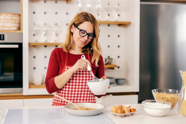 Una mujer de mediana edad revolviendo y preparando una cena en la cocina de su casa