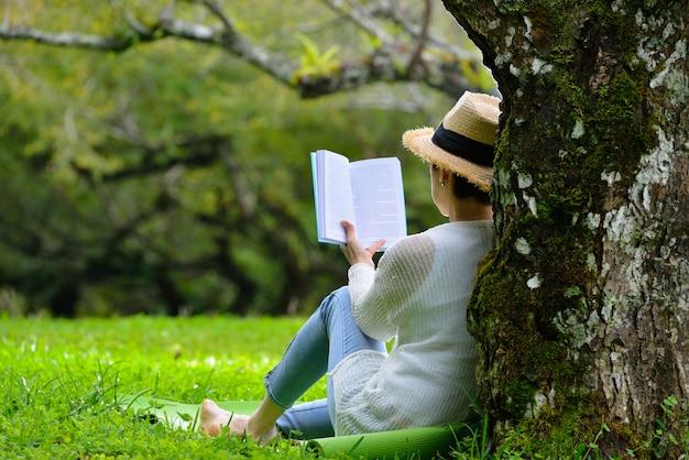 Mujer de mediana edad sentada debajo de un árbol leyendo un libro en el parque