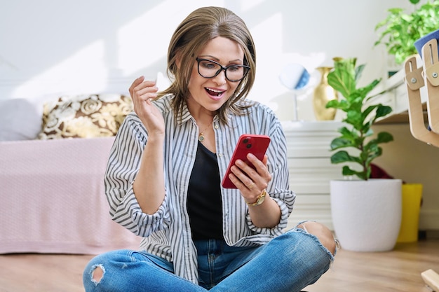 Mujer de mediana edad sentada en el piso en casa con teléfono inteligente