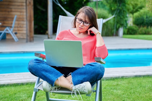 Mujer de mediana edad sentada en una silla en el patio trasero con una laptop