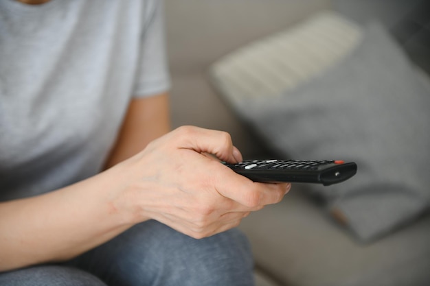 Mujer de mediana edad sentada en el sofá y encendiendo la televisión con un control remoto