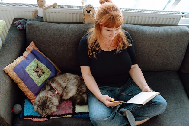 Foto una mujer de mediana edad se sienta en el sofá junto a la ventana con un gato