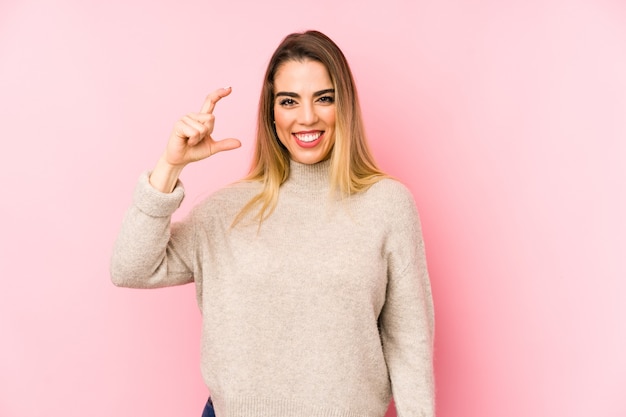 Mujer de mediana edad sobre fondo aislado sosteniendo algo pequeño con los dedos índices, sonriendo y confiado.