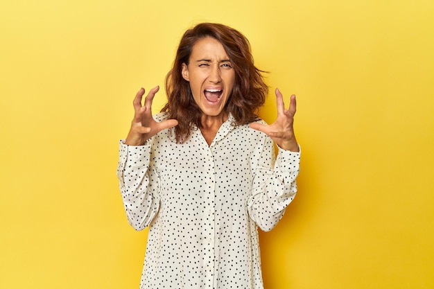 Mujer de mediana edad sobre un fondo amarillo gritando de rabia