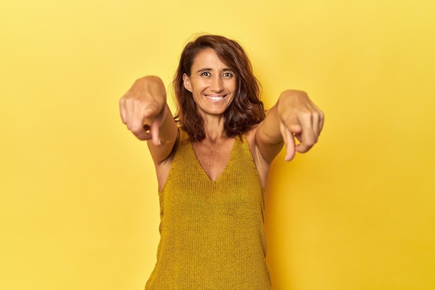 Mujer de mediana edad sobre un fondo amarillo sonrisas alegres apuntando al frente