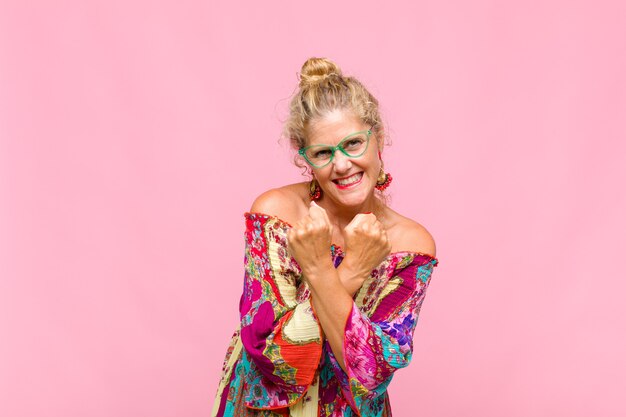 Mujer de mediana edad sonriendo alegremente y celebrando, con los puños apretados y los brazos cruzados, sintiéndose feliz y positiva