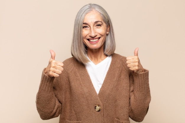 Foto mujer de mediana edad sonriendo ampliamente luciendo feliz, positiva, segura y exitosa, con ambos pulgares hacia arriba