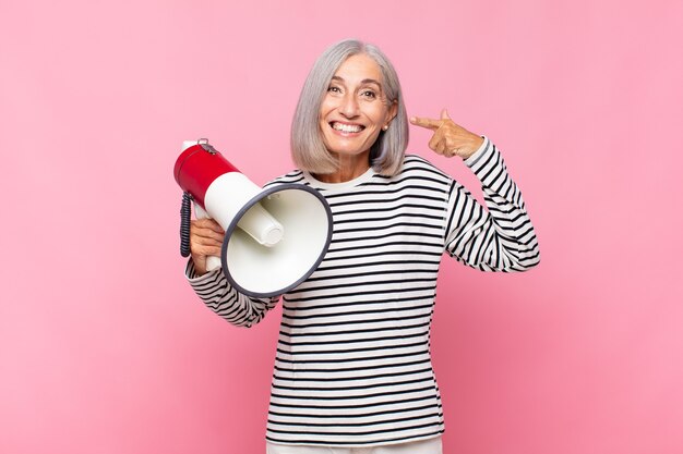 Mujer de mediana edad sonriendo con confianza apuntando a su propia amplia sonrisa