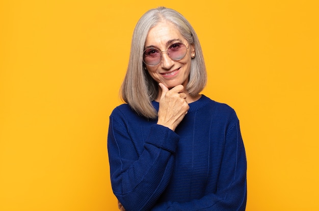 Mujer de mediana edad sonriendo, disfrutando de la vida, sintiéndose feliz, amigable, satisfecha y despreocupada con la mano en la barbilla