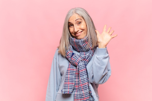 Foto mujer de mediana edad sonriendo feliz y alegremente, saludando con la mano, dándole la bienvenida y saludándolo, o despidiéndose