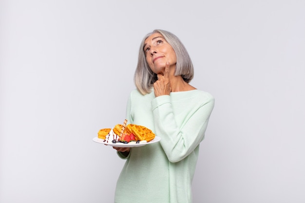 Mujer de mediana edad sonriendo felizmente y soñando despierto o dudando, mirando hacia un lado. concepto de desayuno