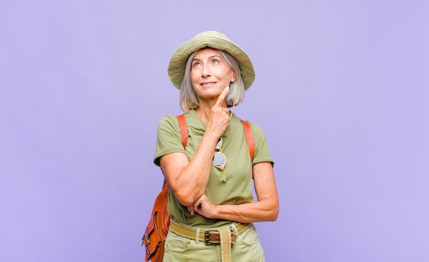 Mujer de mediana edad sonriendo felizmente y soñando despierto o dudando, mirando hacia el lado