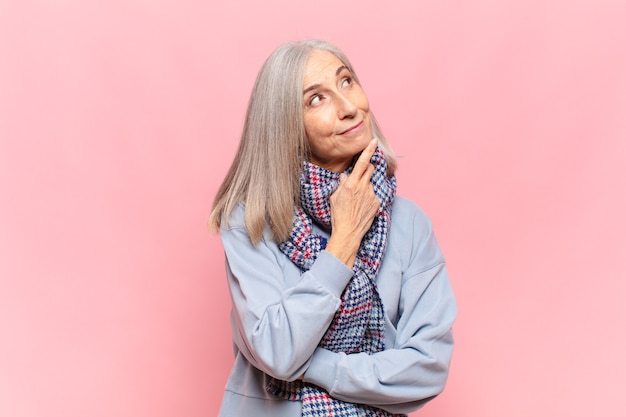 Mujer de mediana edad sonriendo felizmente y soñando despierto o dudando, mirando hacia el lado