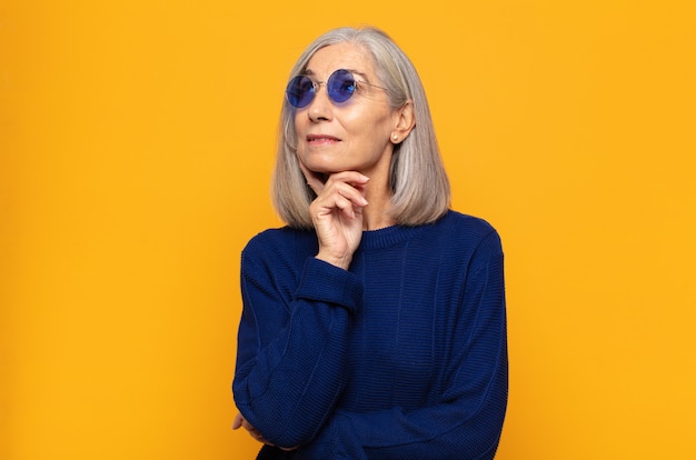 Mujer de mediana edad sonriendo felizmente y soñando despierto o dudando, mirando hacia el lado