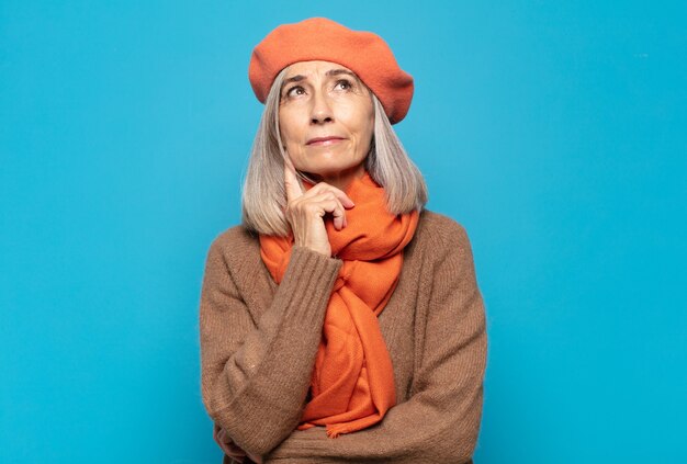 Mujer de mediana edad sonriendo felizmente y soñando despierto o dudando, mirando hacia el lado