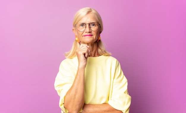 Mujer de mediana edad sonriendo felizmente y soñando despierto o dudando