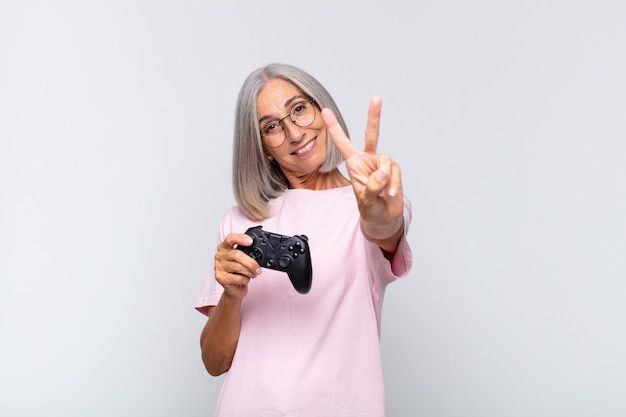 Mujer de mediana edad sonriendo y luciendo feliz, despreocupada y positiva, gesticulando victoria o paz con una mano. jugando concepto de consola