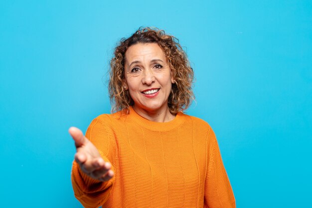 Mujer de mediana edad sonriendo, luciendo feliz, segura y amigable, ofreciendo un apretón de manos para cerrar un trato, cooperando