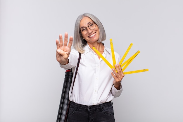 Mujer de mediana edad sonriendo y mirando amigable, mostrando el número cuatro o cuarto con la mano hacia adelante