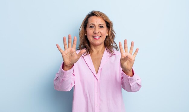 Mujer de mediana edad sonriendo y mirando amistosamente, mostrando el número nueve o noveno con la mano hacia adelante, contando hacia atrás