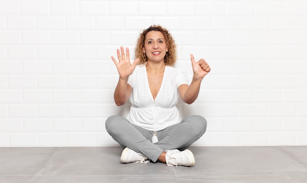 Mujer de mediana edad sonriendo y mirando amistosamente, mostrando el número seis o sexto con la mano hacia adelante, contando hacia atrás