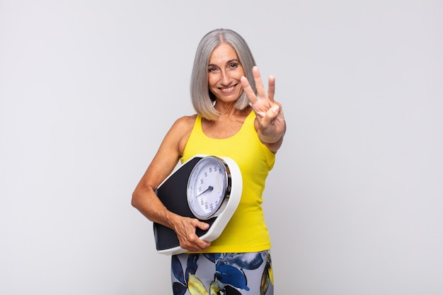 Mujer de mediana edad sonriendo y mirando amistosamente, mostrando el número tres o tercero con la mano hacia adelante