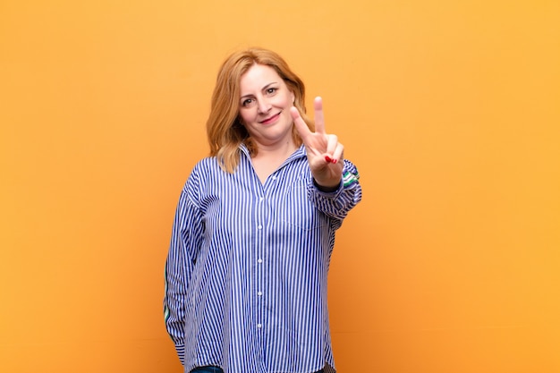 Mujer de mediana edad sonriendo y mirando feliz haciendo gesto de victoria