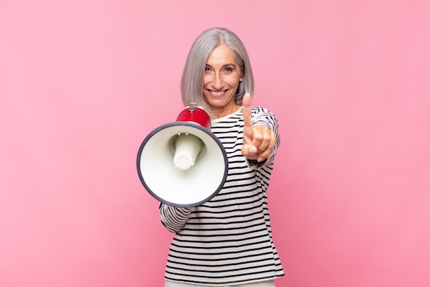 Mujer de mediana edad sonriendo con orgullo y confianza haciendo la pose número uno triunfalmente, sintiéndose como una líder con un megáfono