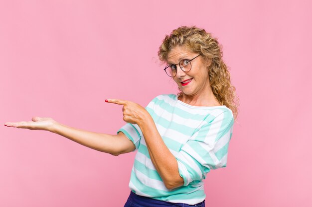 Mujer de mediana edad sonriendo, sintiéndose feliz, despreocupada y satisfecha, apuntando al concepto o idea en el espacio de la copia en el lateral