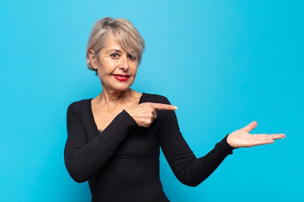 Mujer de mediana edad sonriendo, sintiéndose feliz, despreocupada y satisfecha, señalando el concepto o la idea en el espacio de la copia en el lateral