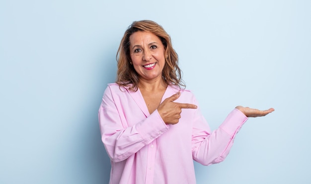 Mujer de mediana edad sonriendo, sintiéndose feliz, despreocupada y satisfecha, señalando el concepto o la idea en el espacio de la copia en el lateral