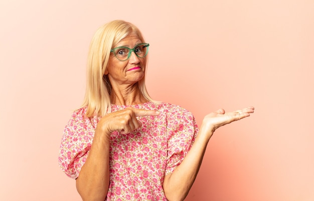 Mujer de mediana edad sonriendo, sintiéndose feliz, positiva y satisfecha, sosteniendo o mostrando un objeto o concepto en el espacio de la copia