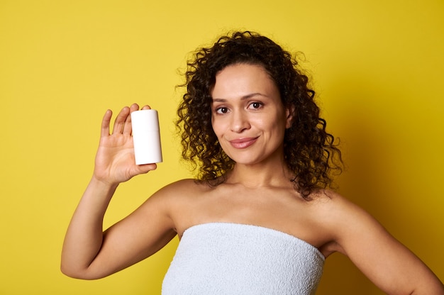 Mujer de mediana edad sosteniendo la botella de producto cosmético aislado sobre fondo amarillo