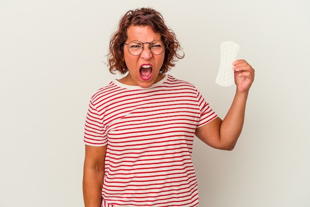Mujer de mediana edad sosteniendo una compresa aislada sobre fondo blanco gritando muy enojado y agresivo.
