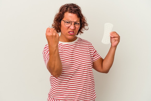 Mujer de mediana edad sosteniendo una compresa aislada sobre fondo blanco mostrando el puño a la cámara, expresión facial agresiva.