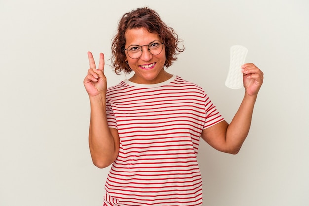 Mujer de mediana edad sosteniendo una compresa aislada sobre fondo blanco que muestra el número dos con los dedos.