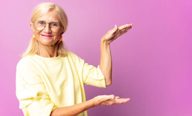 Mujer de mediana edad sosteniendo un objeto con ambas manos en el espacio de copia lateral, mostrando, ofreciendo o publicitando un objeto