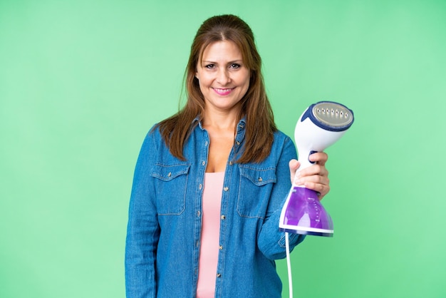 Mujer de mediana edad sosteniendo una plancha sobre un fondo aislado con expresión feliz