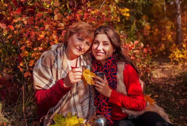 Mujer de mediana edad y su hija tomando un té en el bosque de otoño